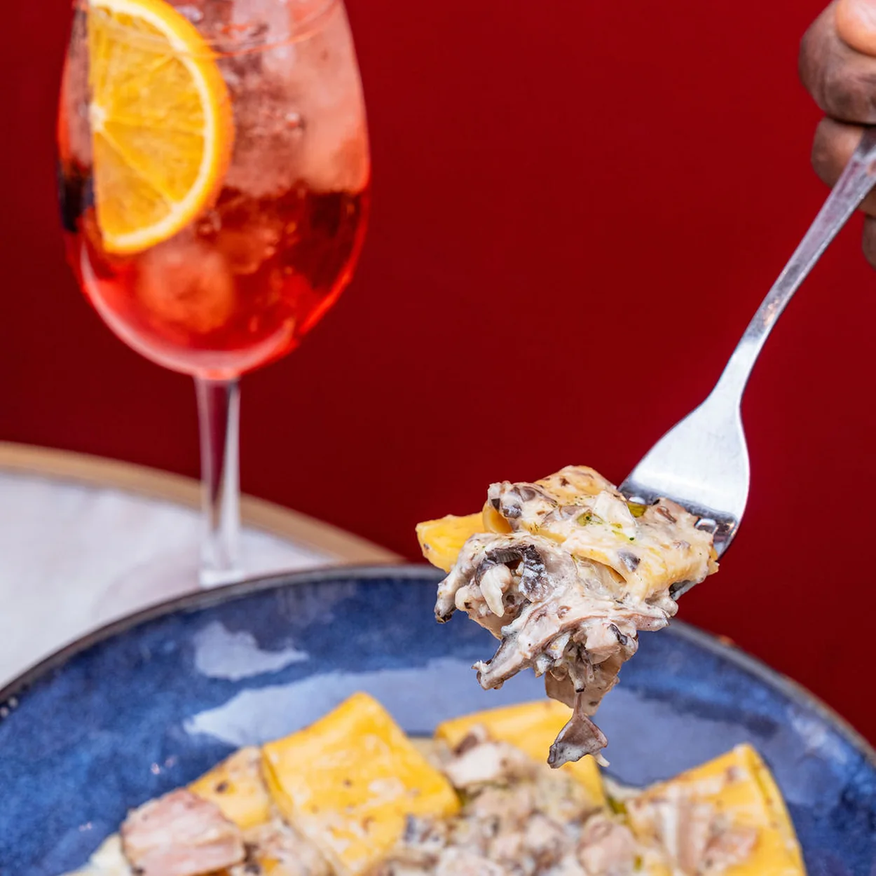Fork lifting mushroom ravioli beside an orange-garnished spritz at 27 Old Compton Street