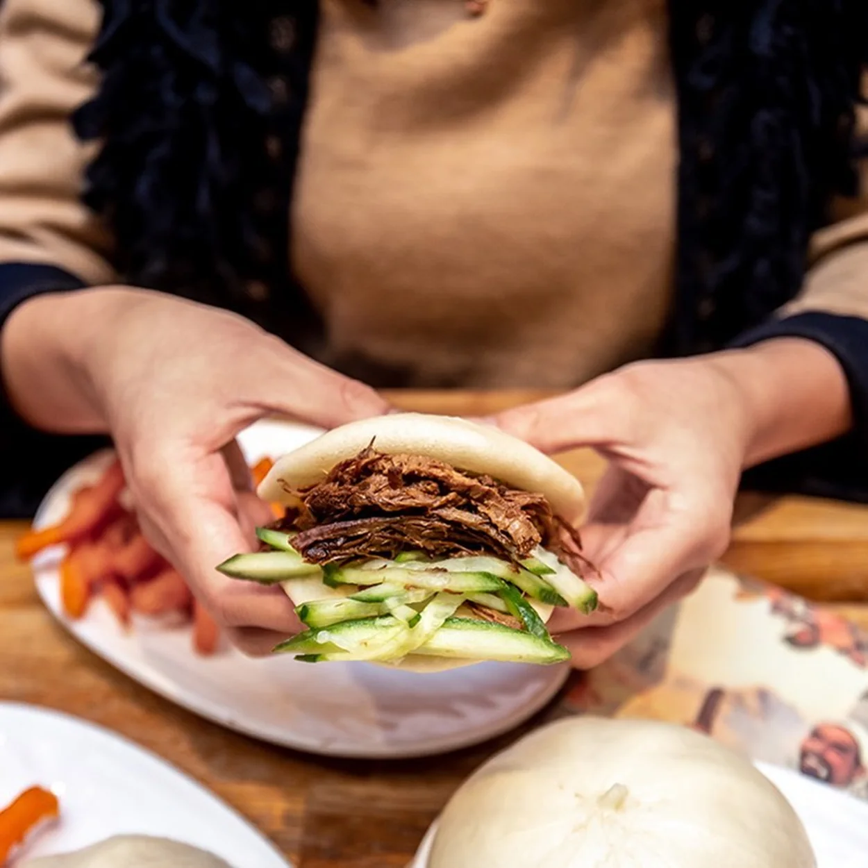 Hands holding a filled baozi bun over a plate at Baozi Inn on Romilly Street