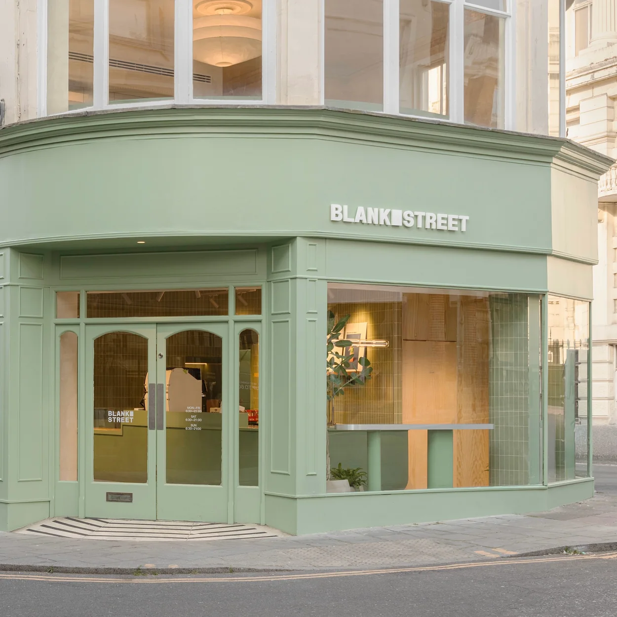 Corner facade of a Blank Street Coffee shop painted in the brand's sage green