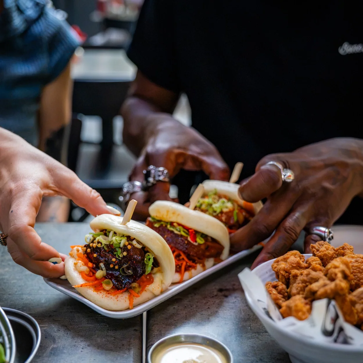 Hands serving bao buns and fried chicken at Bone Daddies in Soho