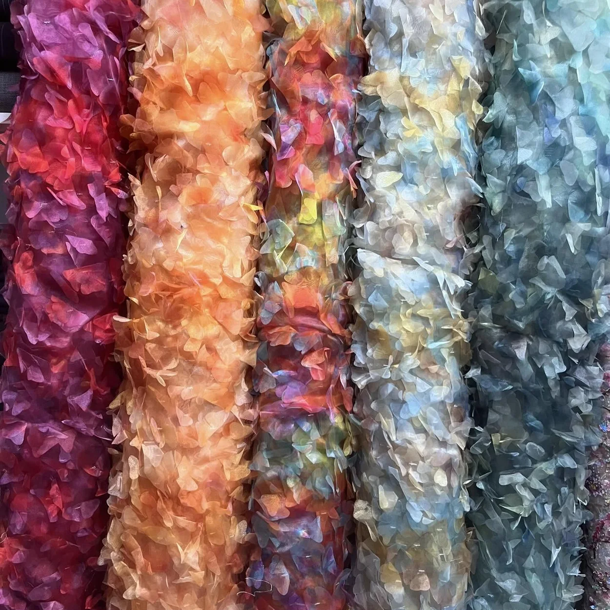 Rolls of textured petal fabrics in orange, pink and blue at Borovick Fabrics