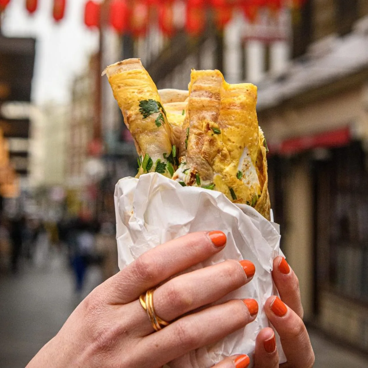 Egg waffle roll held up beneath the lanterns outside Chinese Tapas House in Chinatown