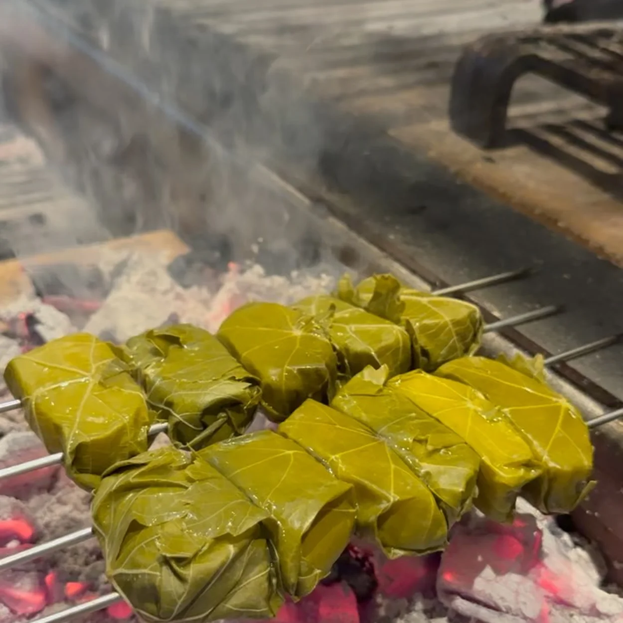 Leaf-wrapped skewers cooking over glowing charcoal at Impala Soho