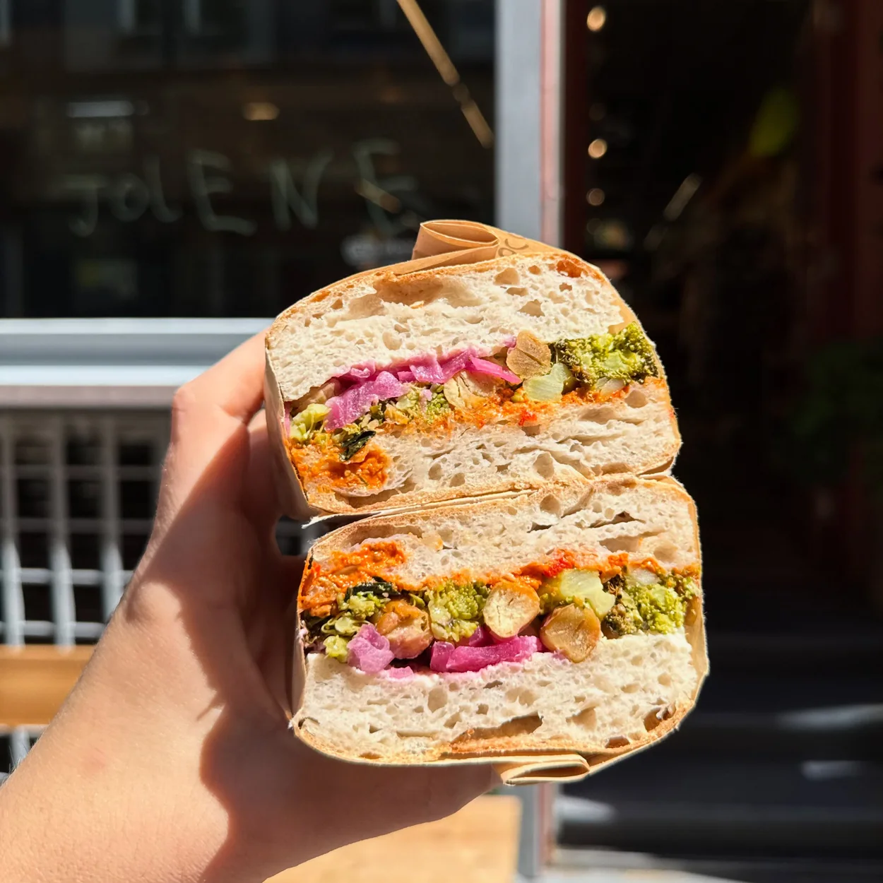 Stuffed focaccia sandwich with pickled cabbage held up outside Jolene Soho