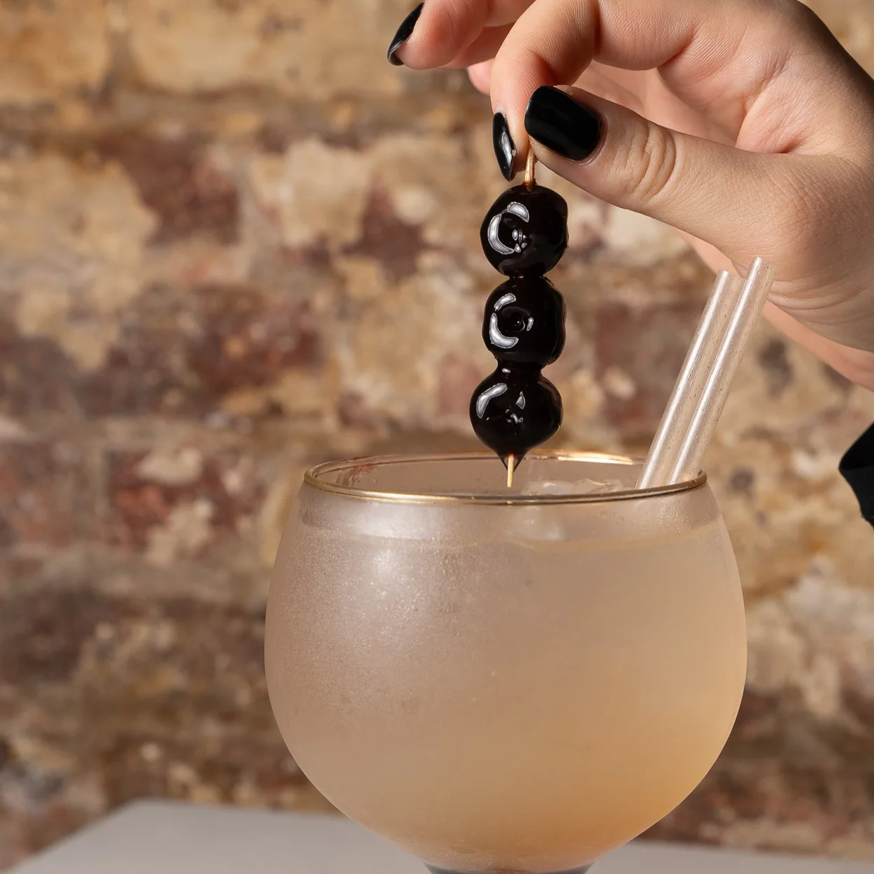 Cocktail garnished with dark cherries against the exposed brick bar at My Place Soho