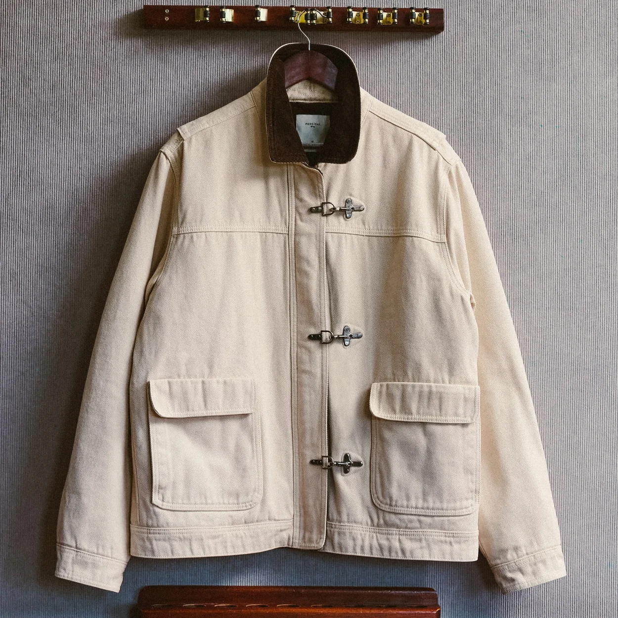 Cream workwear jacket hung on a wooden rail, part of Percival's Soho menswear range