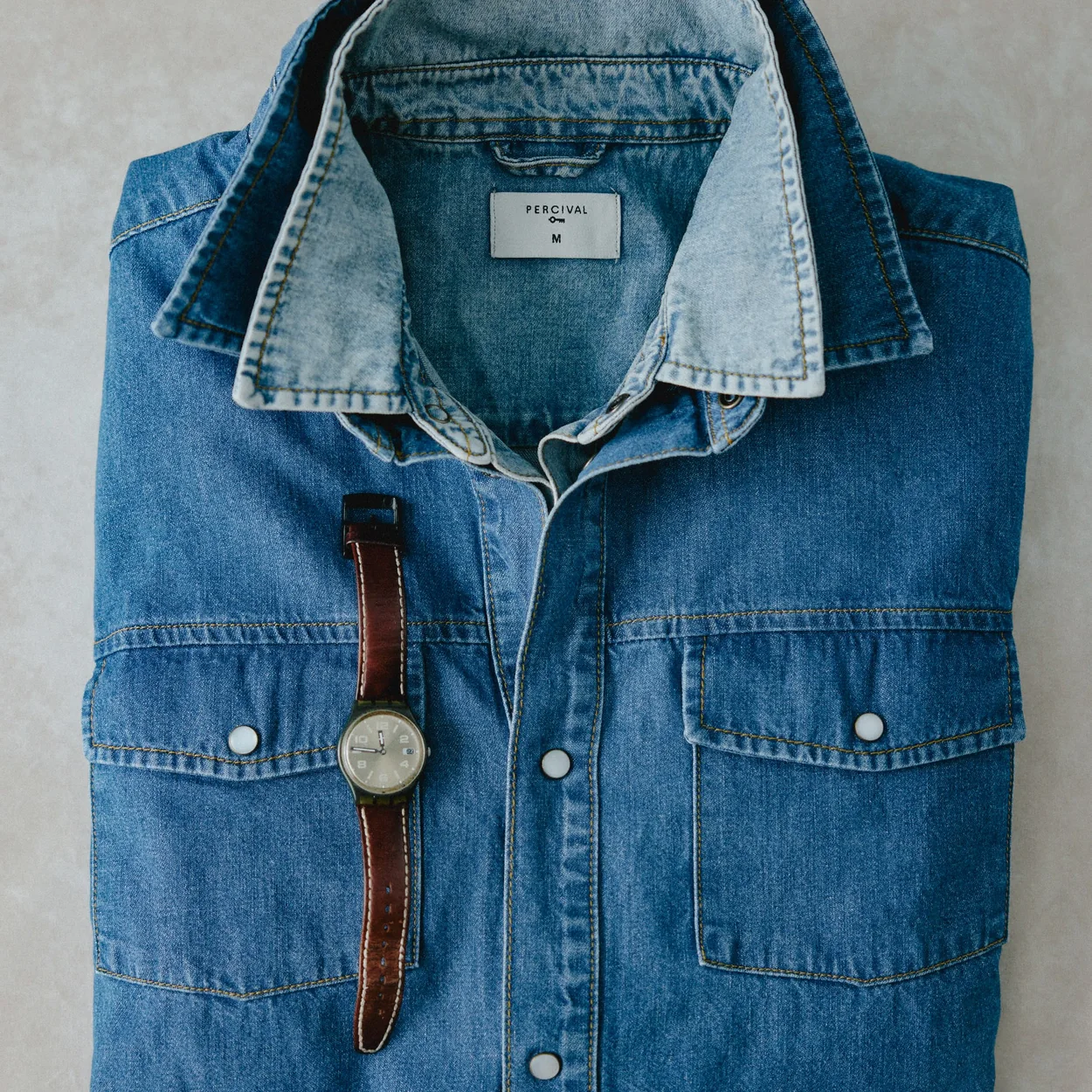 Denim shirt flat lay with a leather-strapped watch from Percival's Soho store