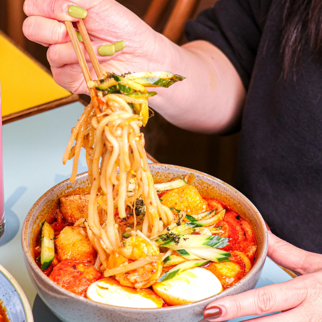 Lifting noodles from a bowl of curry laksa at Rasa Sayang in Chinatown