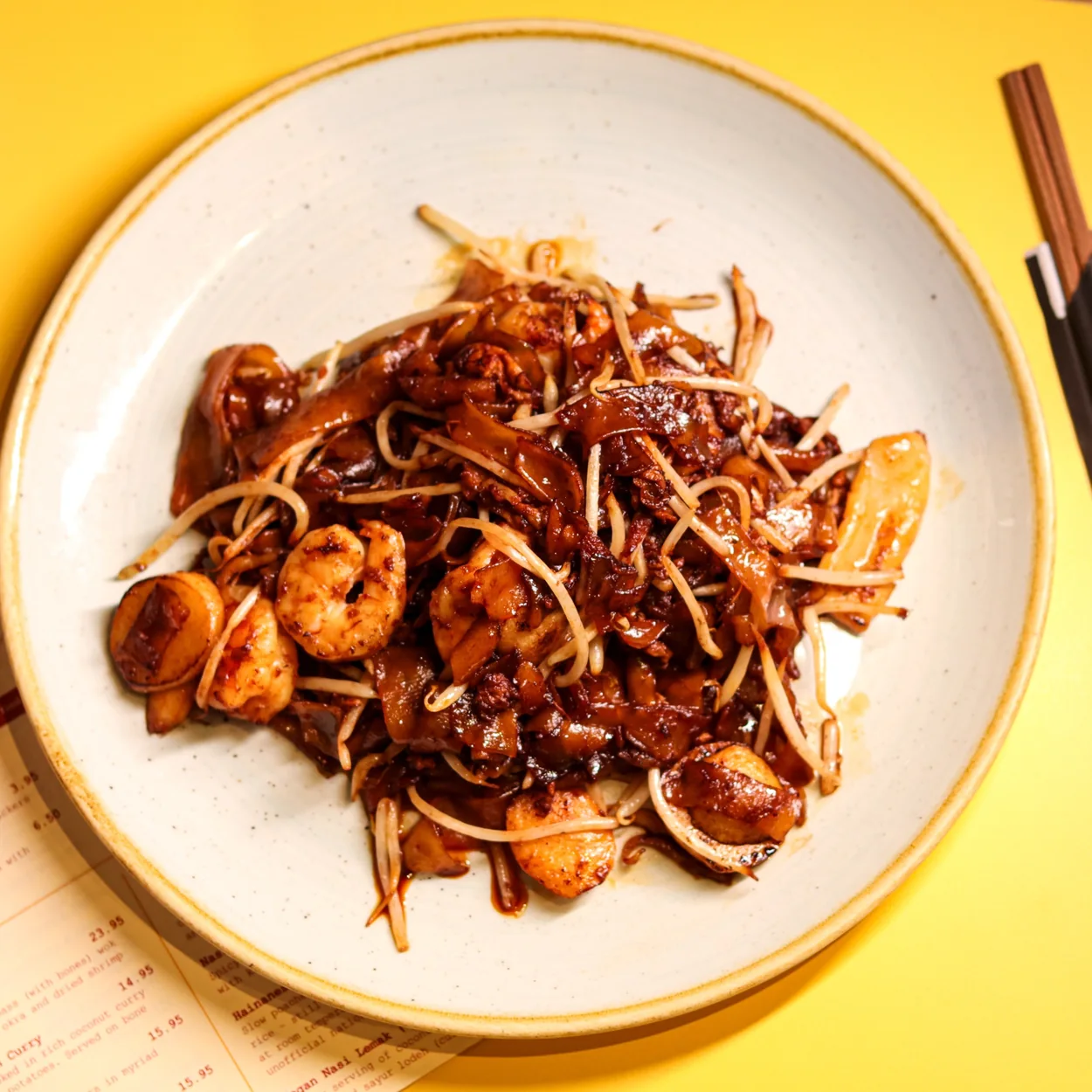 Char kway teow served on the yellow tables at Rasa Sayang London
