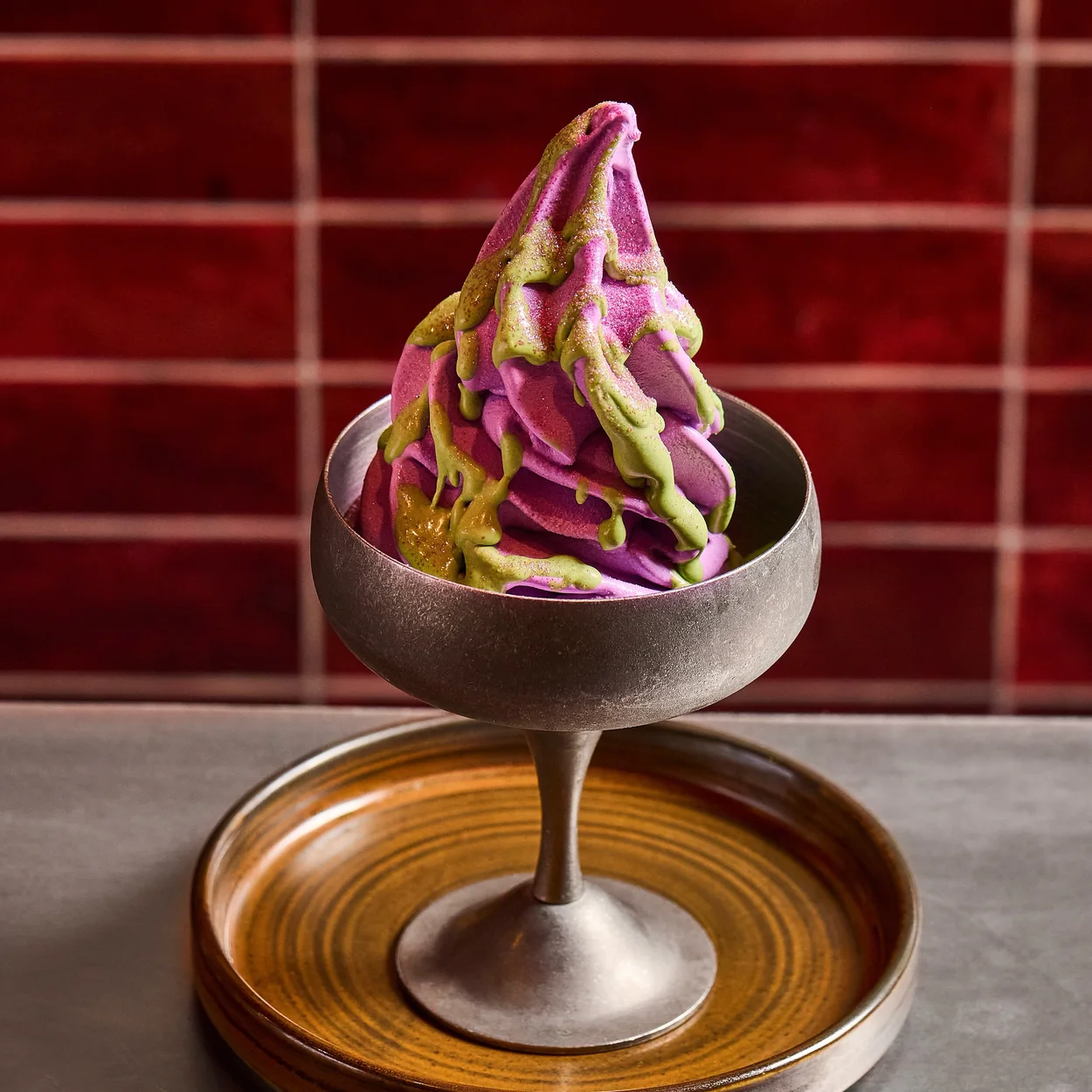 Purple and green soft serve swirl in a metal coupe against Tangra's red tiles