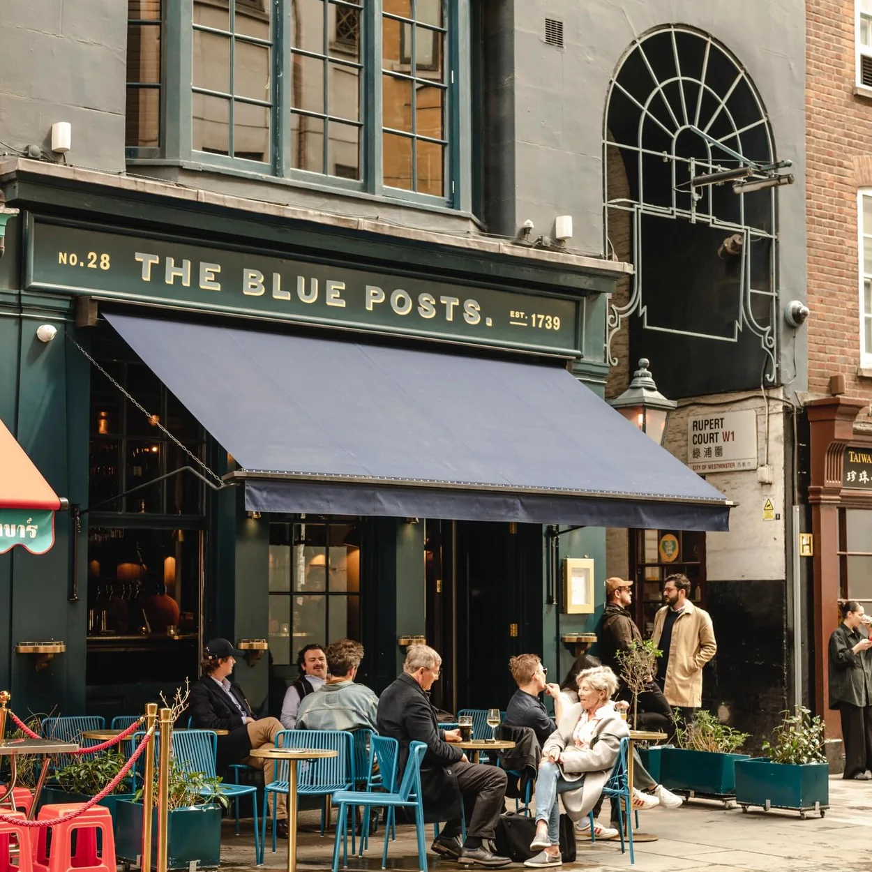 The Blue Posts pub frontage on Rupert Street with its navy awning and pavement drinkers