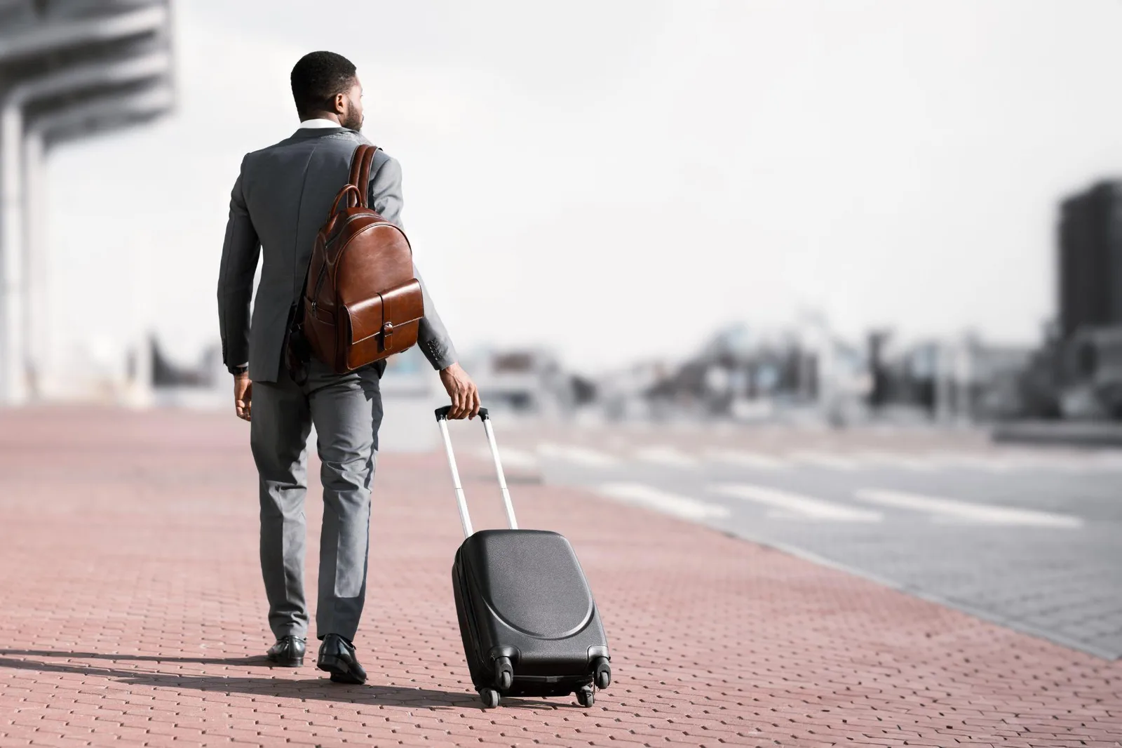 Business traveller in a suit walking with cabin luggage and a leather backpack