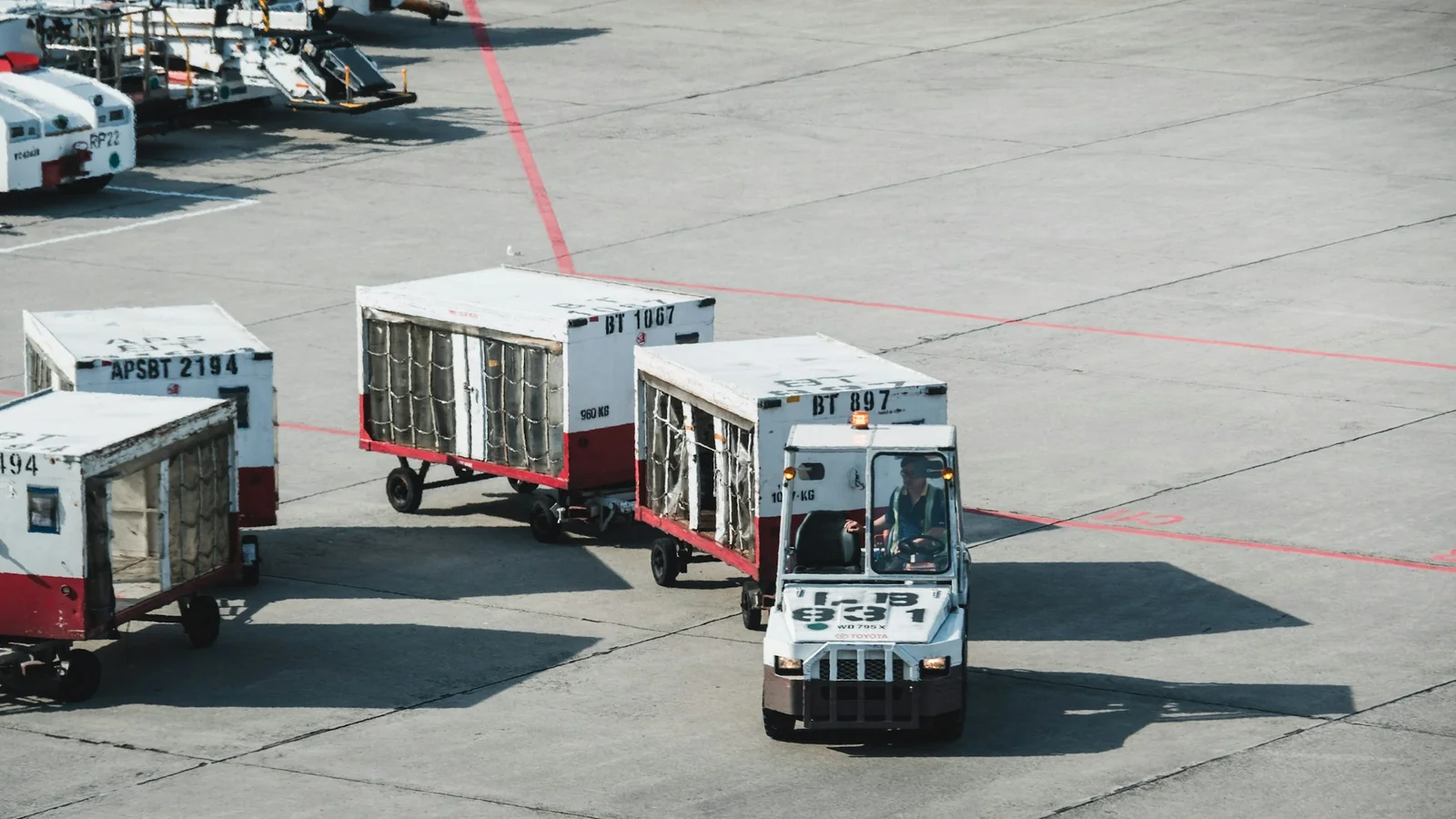 Airport ground crew towing loaded cargo dollies across the apron, the handling stage that decides whether an urgent shipment keeps its schedule