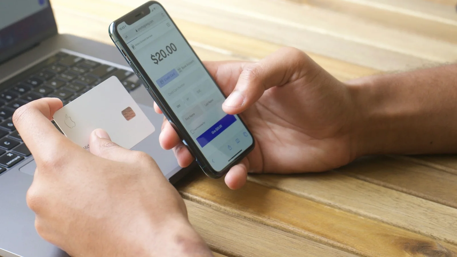 Hands holding a payment card and a phone showing a checkout form with the card fields and the confirm button on screen